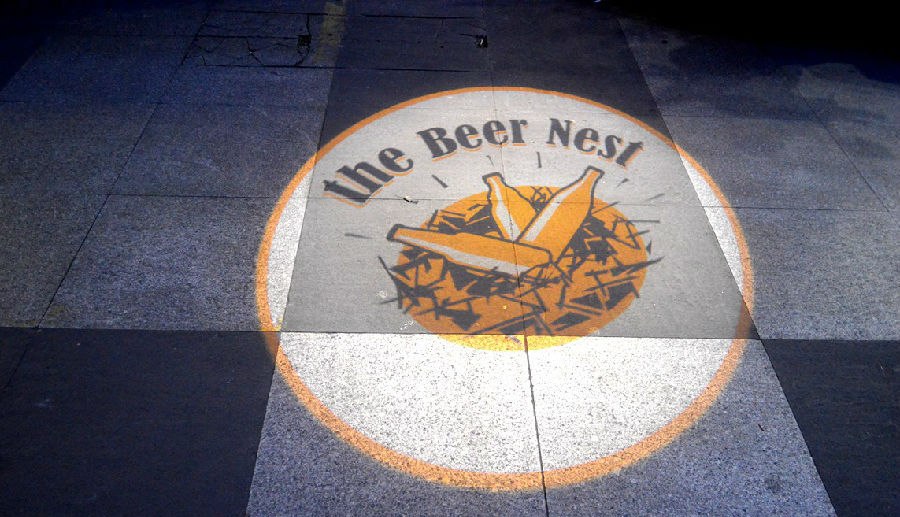 人行道上,一圈灯光打出 The Beer Nest 的圆形招牌